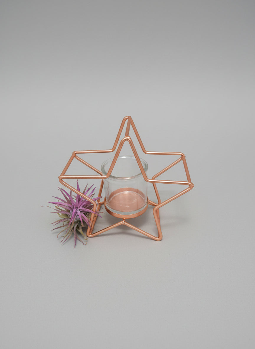 Star-shaped gold candle holder with a purple candle on a beige surface